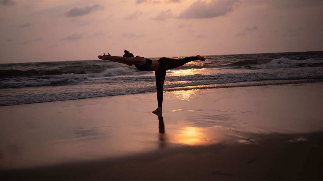 Yoga im Krieger drei am Strand im warmen Abendlicht